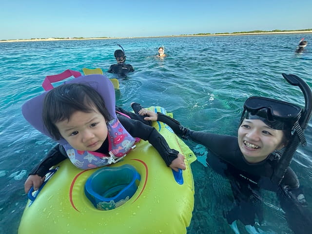 幼児のお子様と一緒に浮き輪を使って沖縄の海を楽しんでいる様子